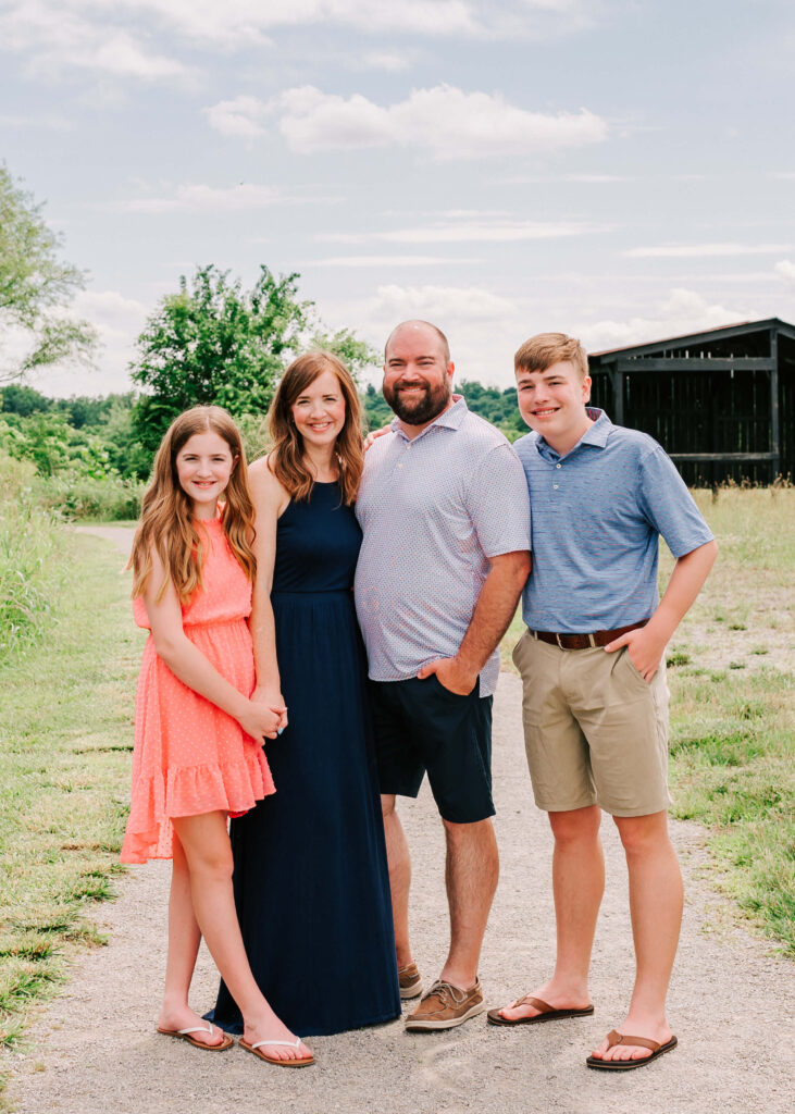 Family of four in blue and coral color scheme smiling on a farm