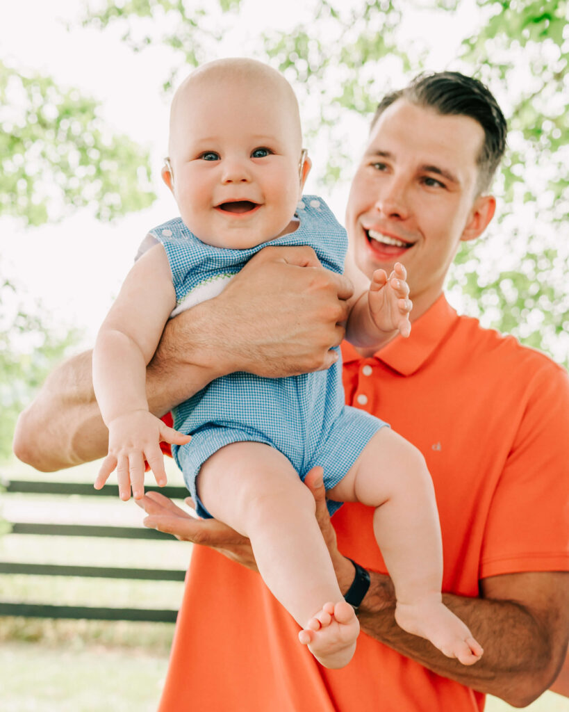 dad in orange holding his baby and laughing 
