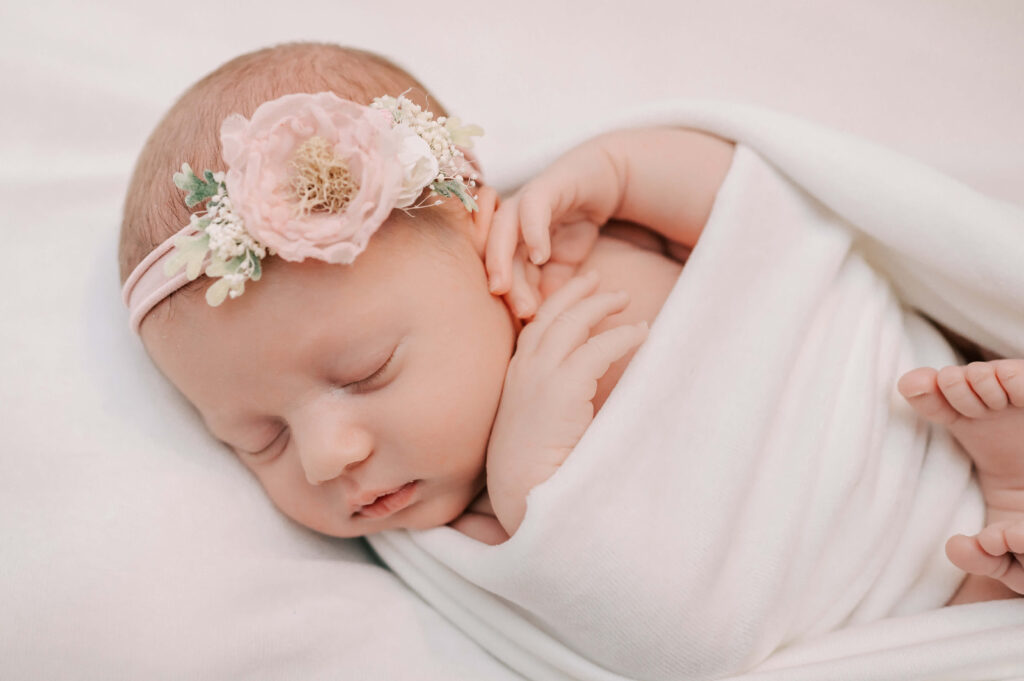 newborn girl wrapped in white with a flower headband